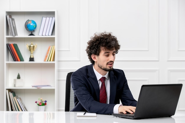 Customer service curly brunette young man in office suit with laptop typing