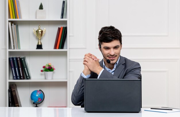 Customer service cute guy in grey suit with computer and headset making a deal happily