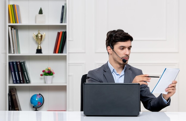 컴퓨터와 헤드셋이 메모를 가리키는 회색 양복을 입은 고객 서비스 귀여운 남자