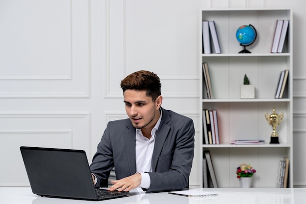 Customer service cute handsome guy in office suit with computer typing on keyboard