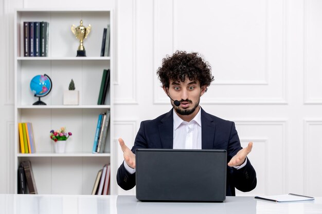 Customer service handsome curly man in office suit with computer and headset confused