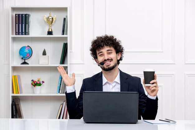 Customer service handsome curly man in office suit with computer headset smiling holding coffee