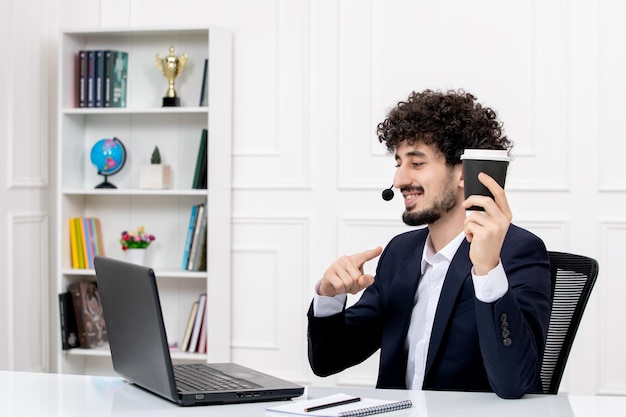 Free photo customer service handsome curly man in office suit with computer and headset smiling with coffee