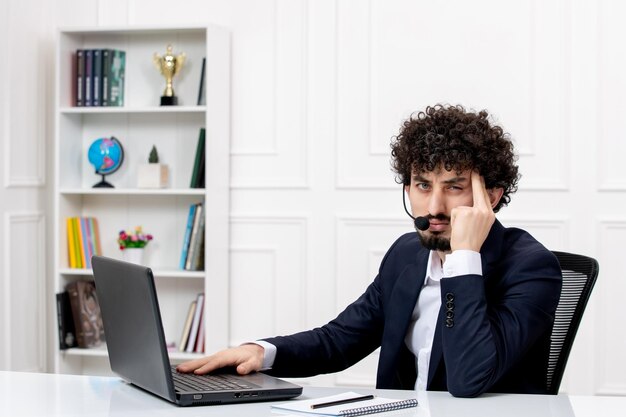 Customer service handsome curly man in office suit with computer and headset tired and annoyed