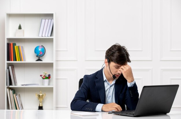 Customer service handsome guy with headset and laptop in suit thinking and touching forehead