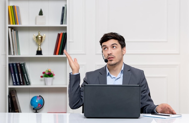 Customer service handsome man in grey suit with computer and headset waving hands