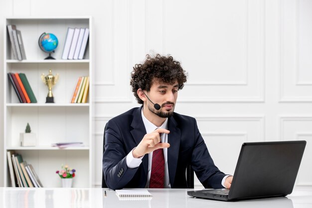 Customer service handsome young guy in office suit with laptop and headset talking on videocall