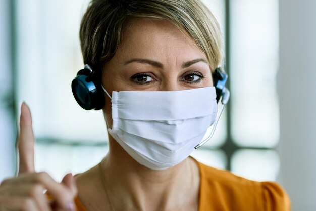 Customer service operator with raised index finger wearing face mask and looking at the camera