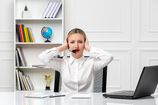 Customer service pretty blonde girl in white shirt with laptop and headset holding temples