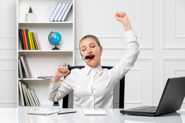 Customer service pretty blonde girl in white shirt with laptop and headset tired and yawning