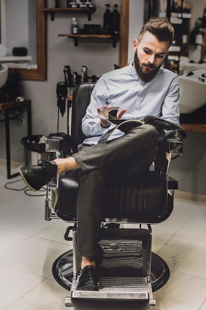 Foto gratuita cliente che guarda la rivista nel negozio di barbiere