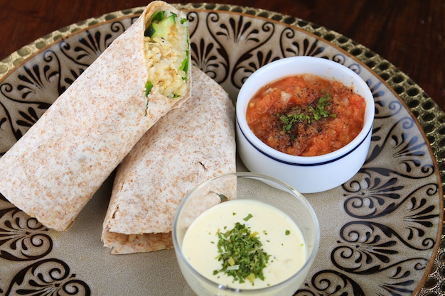 Cut burrito with white and red sauces served in a plate with patterns