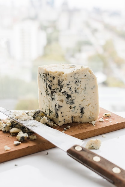 Cut cheese with knife on wooden chopping board over the white table