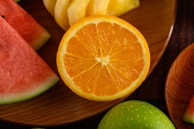 Cut watermelons, oranges and pineapples on a wooden plate with apples