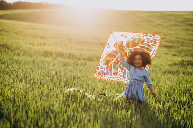 Cute african baby girl at the field on the sunset playing with kite