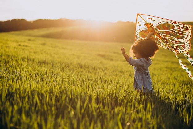 Милая африканская девочка на поле на закате, играя с воздушным змеем