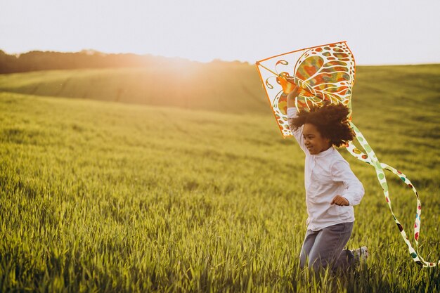 Милая африканская девочка на поле на закате, играя с воздушным змеем