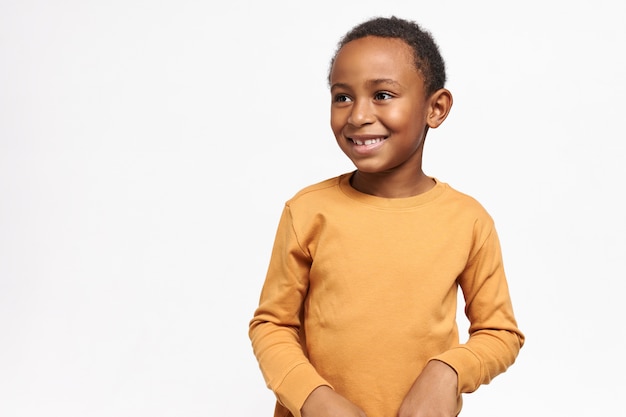 Cute afro american schoolboy in yellow sweatshirt posing against white wall with copy space for your information