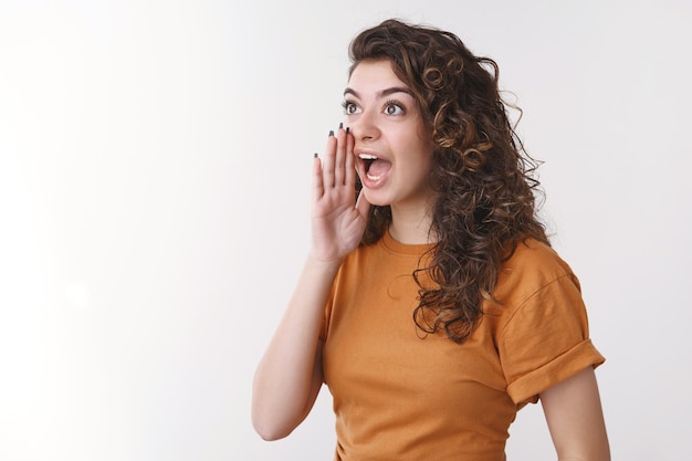 Cute armenian curly-haired girl yelling loud turn left hold palm open mouth calling brother come down dinner ready standing white background shouting searching friend crowded party