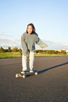 Foto gratuita ragazza asiatica sveglia che guida skateboard che pattina sulla strada e pattinatore sorridente sul longboard dell'incrociatore che gode di o