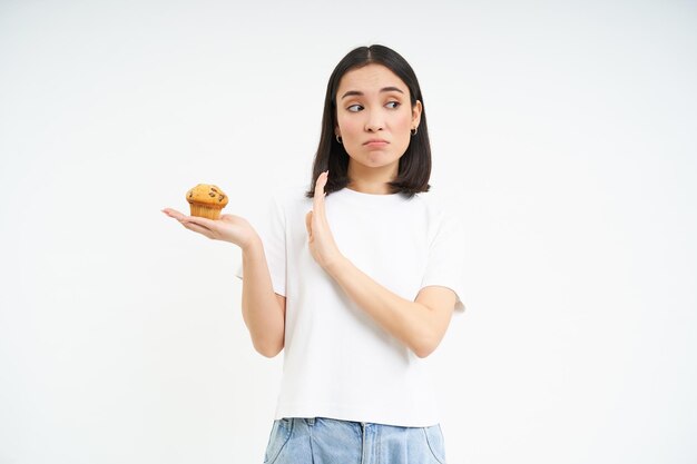 Cute asian girl with will power refuses the cupcake stays on diet isolated on white background