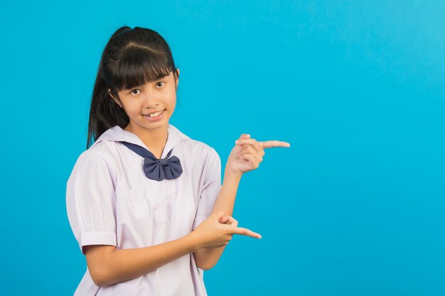 Cute Asian schoolgirl doing two hands pointing gesture on a blue .