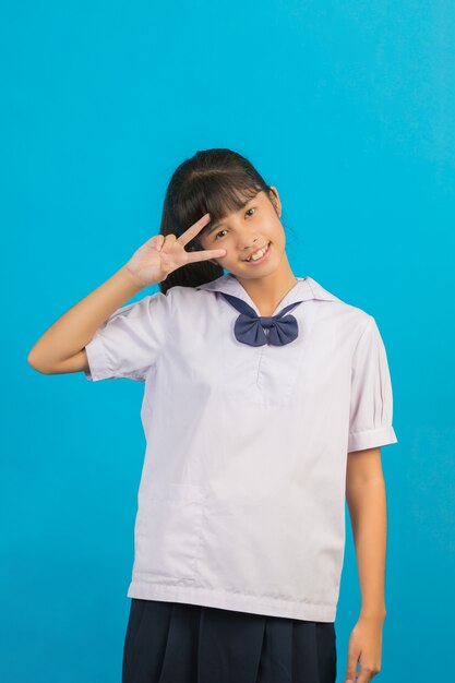 Cute Asian schoolgirl showing two fingers on a blue .