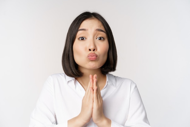 Cute asian woman begging say please asking for favour need help standing with coy face against white background