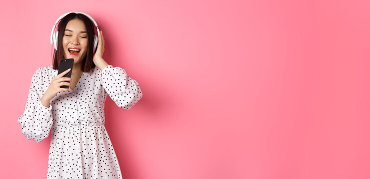 無料Photo 携帯電話で歌ってカラオケ アプリを再生し、ドレスに立ってヘッドフォンを使用してかわいいアジアの女性