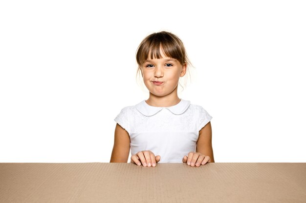Cute and astonished little girl opening the biggest postal package. Excited young female model on top of cardboard box looking inside.