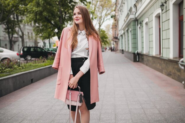ピンクのコートで街を歩くかわいい魅力的なスタイリッシュな笑顔の女性