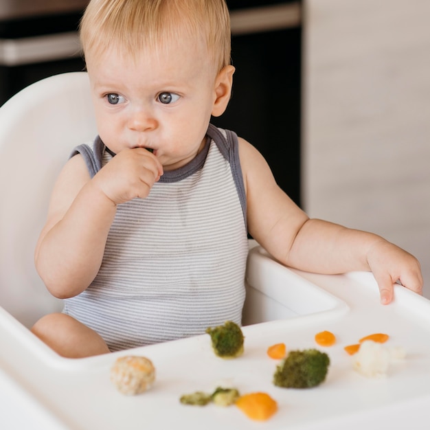 Милый мальчик в детском стульчике ест овощи
