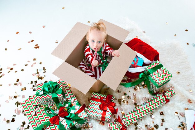 Милая девочка 1 год, сидящая в коробке на фоне рождественских украшений. Праздник, праздник, детская концепция