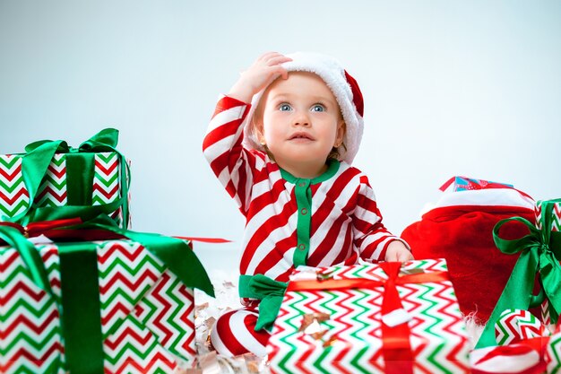 Милая девочка 1 года в шляпе санта-клауса позирует над рождественскими украшениями