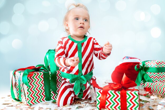 クリスマスの背景にポーズをとってサンタ帽子の近くのかわいい女の赤ちゃん。クリスマスボールと床に座っています。連休シーズン。