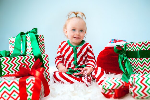 Cute baby girl near santa hat posing over Christmas background with decoration. Sitting on floor with Christmas ball.