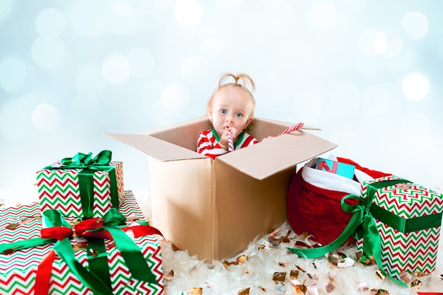 Cute baby girl sitting in box over Christmas background. Holiday, celebration, kid concept