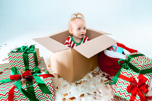 Neonata sveglia che si siede nella casella sopra il fondo di natale. vacanza, celebrazione, concetto di bambino