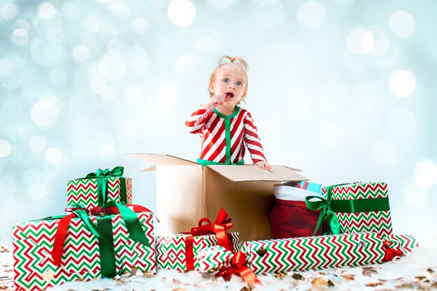 クリスマスの背景の上のボックスに座っているかわいい女の赤ちゃん。休日、お祝い、子供の概念