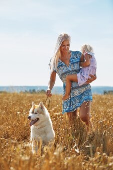 麦畑​で​ママ​と​犬​と​かわいい​女​の​赤ちゃん​。​幸せな​若い​家族​は​自然​の​中​で​一緒​に​時間​を​楽しんでいます​。​ママ​、​小さな​女​の​赤ちゃん​、​犬​の​ハス​キー​が​屋外​で​休んでいます​。​一体感​、​愛​、​幸福​の​概念​。