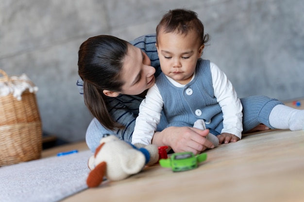 Foto gratuita bambino sveglio che gioca sul pavimento con il giocattolo e sua madre