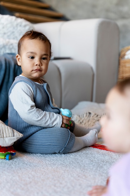 Bambino carino che gioca sul pavimento con il giocattolo mentre il bambino sfocato è seduto sul pavimento