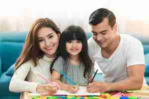 免费照片可爱黑色的头发孩子女女儿作业,笑与父母一起在起居室的房子里的概念
