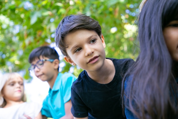 Cute black haired boy enjoying outdoor activities, playing with friends in park. Group of children having fun outdoors. Childhood concept