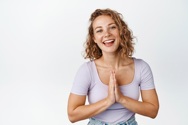 Foto gratuita ragazza bionda carina che dice grazie e inchinandosi con il segno di namaste, sorridendo e ridendo felice, in piedi su sfondo bianco