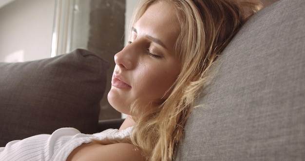 Free photo cute blond girl sleeping peacefully on a gray couch in soft daylight