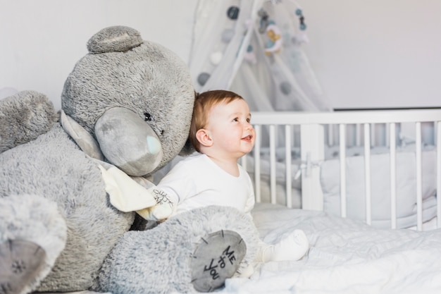 Cute blonde baby in white bed with teddy bear