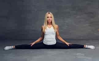 Free photo cute blonde female sits in legs spilt over grey background.