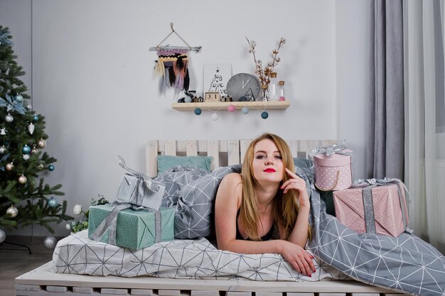스튜디오에서 새 해 나무에 대 한 선물 상자와 함께 침대에 누워 검은 브래지어에 귀여운 금발 소녀 해피 홀리데이