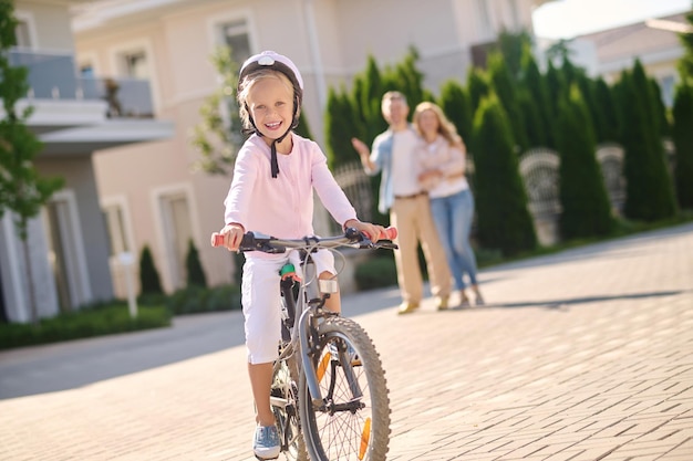 A cute blonde girl learning to ride a bike with her parents